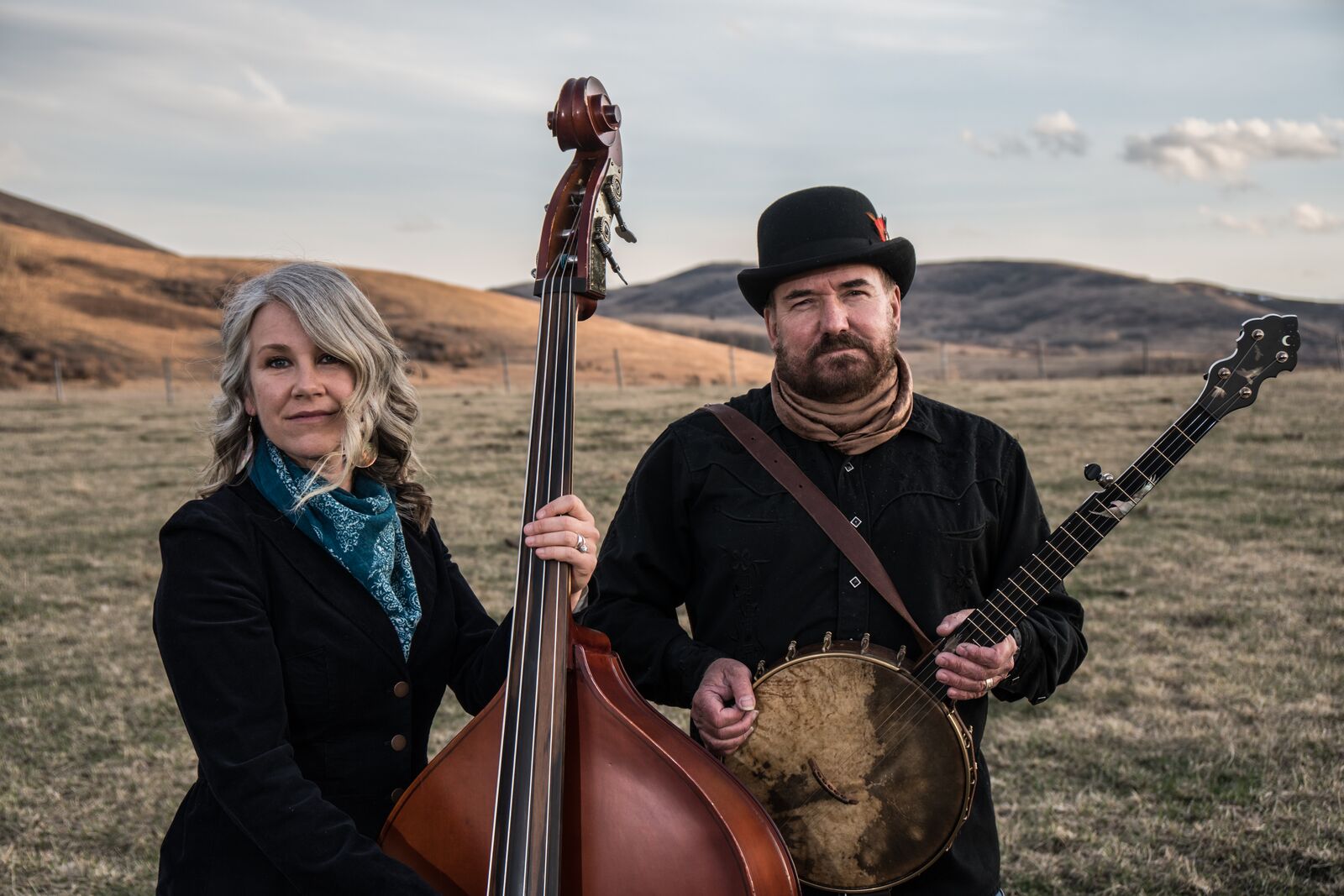 With the background of the Alberta foothills, a woman stands with her double bass and a man stands to her right with a guitar